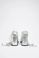 Zapatos de tacón plateados con plataforma, punta cuadrada, tiras cruzadas y cordones para atar al tobillo.