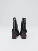 Botas de cuero negro con punta cuadrada, taco ancho de madera y costura decorativa bordada en contraste a lo largo del empeine. Cuenta con cierre en la parte trasera.
