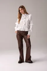 Camisa celeste con volados decorativos en los hombros, pecho, mangas y ruedo, destacados con ribetes en tono rojo. Presenta cierre frontal de botones, cuello alto y mangas largas abullonadas con puños ajustados.