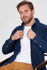 Camisa de jean celeste de manga larga, con cuello clásico, cierre frontal con botones a presión, dos bolsillos con solapa abotonada en el pecho, corte en hombros y detalle en la espalda.