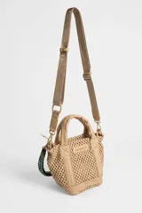 Cartera Rapsodia tipo tote mini en color tostado, confeccionada con cuerpo de tejido estilo red y detalles en material sintético liso. Cuenta con asas de mano acolchadas y una correa desmontable trenzada en tonos verde, rosa y marrón con herrajes metálicos. Incluye una placa frontal con el nombre de la marca grabado.