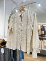 Camisa negra con cuello alto, mangas largas abullonadas y cierre frontal con botones. Presenta detalles de encaje y lentejuelas en el frente.