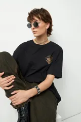 Remerón unisex negro de manga corta y cuello redondo, con pequeño estampado lateral en el frente con forma de flor y rayos.