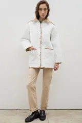 Campera acolchada de corte holgado, color blanco con diseño capitoneado en forma de rombos. Presenta cuello camisero y bordes internos con estampado floral en tonos azul y rojo, cierre frontal con botones a presión y bolsillos laterales.