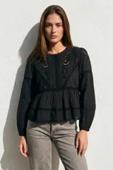 Blusa negra de algodón con diseño de broderie y calados en el pecho y hombros. Presenta corte oversize, mangas largas con puños y un detalle de volado en la cintura.