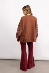 Buzo negro de cuello redondo con diseño de flores bordadas en las mangas. Presenta un corte holgado y puños elásticos.