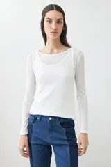 Remera de manga larga, color blanco roto, con cuello bote y textura acanalada. Presenta un efecto de doble capa o transparencia sutil en el escote.