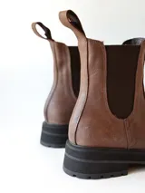 Bota tipo Chelsea de cuero color chocolate, con paneles elásticos laterales, tirador trasero y suela track negra de goma.