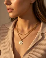 Collar doble de acero con baño de oro, compuesto por una cadena de eslabones finos y una segunda cadena con un dije circular grabado con el símbolo Hamsa.