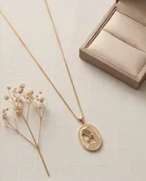 Collar de bronce dorado con cadena fina y dije ovalado con la figura de una virgen incrustada con pequeños cristales y una perla central.