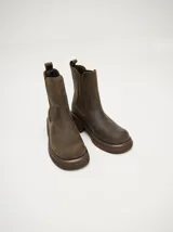 Bota tipo Chelsea de caña media, confeccionada en cuero vacuno negro con acabado mate. Presenta paneles laterales elásticos, tirador trasero y una suela robusta con plataforma delantera y taco cuadrado.