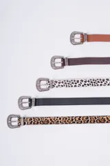 Cinturón de estilo western con hebilla metálica plateada ornamentada. Disponible en varios colores y estampados: cuero marrón claro, cuero marrón oscuro, estampado dálmata (blanco y negro) y cuero negro liso. También disponible en estampado leopardo.