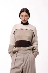 Sweater de tejido de punto grueso con diseño de bloques de color en tonos beige, marrón y bordó. Presenta un corte relajado, mangas amplias y detalles de costuras visibles en contraste que separan las franjas de color.