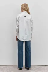 Camisa de corte clásico y calce holgado, color blanco, con cuello camisero, cierre frontal de botones y mangas largas con puños abotonados.