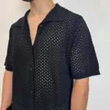 Camisa de tejido de punto calado en color beige, con cuello polo, cierre frontal de botones y mangas cortas.