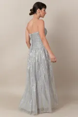 Vestido largo de tul bordado color gris claro, con lentejuelas plateadas y doradas. Modelo strapless drapeado y falda con movimiento.