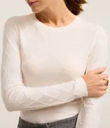 Suéter de punto color blanco con cuello redondo y mangas largas. Presenta una textura geométrica de losangos en toda la prenda y un corte ajustado al cuerpo.