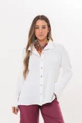 Camisa blanca de manga larga con cuello camisero, cierre frontal abotonado y puños anchos abiertos. Presenta un diseño clásico y versátil.