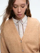 Cardigan de punto color beige con cierre frontal de botones, cuello en V y dos bolsillos delanteros. Presenta mangas largas con puños acanalados y un diseño de corte holgado.