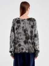 Buzo de punto con diseño jaspeado en tonos gris y negro, de cuello amplio y corte holgado. Confeccionado en una mezcla de mohair y lana que le otorga una textura suave y afelpada.
