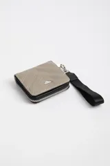 Billetera cuadrada color gris topo, con diseño capitoneado en diagonal, cierre perimetral con cremallera negra, tira de agarre de mano y logo triangular metálico.