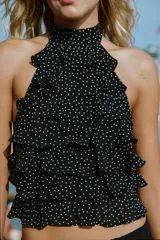 Top de cuello halter color blanco, con múltiples volantes en cascada en todo el frente y la espalda descubierta con cierre de botones y lazada en el cuello.