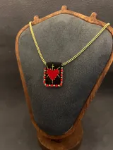 Collar con cadena dorada y dije rectangular de tela negra bordado a mano con un corazón rojo y detalles en hilo dorado, bordeado con mostacillas rojas.