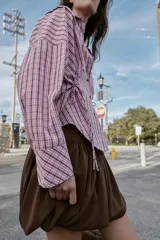 Camisa de manga larga con estampado de cuadros en tonos rosados y negros. Presenta cuello solapa, bolsillo delantero de plastrón, cierre frontal con botones y detalle de laterales ajustables con lazos.