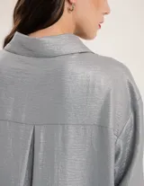 Camisa oversized con terminación metalizada color gris plomo. Tiene botones a tono en el delantero, largo por debajo de la cadera y tajos a los costados.