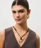 Conjunto de bijouterie compuesto por collar con cordón negro ajustable y dije colgante de metal dorado con diseño orgánico, acompañado de caravanas a juego.