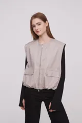 Chaleco color caqui con cierre frontal con cremallera, bolsillos con solapa y corte holgado.