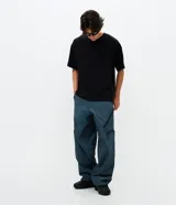 Pantalón de corte holgado en color azul petróleo, confeccionado en microfibra de poliéster. Presenta un diseño utilitario con múltiples bolsillos funcionales, cierres visibles y detalles técnicos en las piernas.