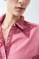 Camisa de corte clásico y manga larga en tono celeste claro, con diseño de estrellas aplicadas en tejido desflecado. Presenta cuello camisero y cierre frontal con botones.