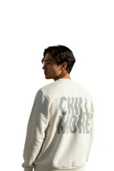 Buzo de felpa color beige con cuello redondo, mangas largas y estampa grande en la espalda con la frase "Chill More" en tonos grises.