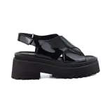 Sandalias de plataforma Korium modelo Della, de color negro con acabado charol. Presentan tiras anchas cruzadas en el empeine y tira ajustable con hebilla en el talón, sobre una suela gruesa track dentada.