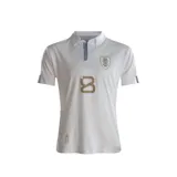 Camiseta de fútbol blanca de la Selección Uruguaya, modelo alternativo 2024. Diseño con cuello polo abotonado y detalles en azul y dorado. Incluye escudo de la AUF, logo de la marca y leyenda conmemorativa.