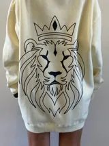 Hoodie oversize color crema, con capucha ajustable mediante cordones y bolsillo frontal tipo canguro. Presenta un diseño estampado de un león en la espalda.