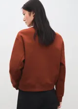 Jersey de punto liso en color marrón terracota, con cuello redondo y diseño de manga larga con puños y bajo de canalé.