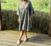 Vestido corto de lino color beige claro, con cuello mao, escote con botones de nácar, mangas tres cuartos con volados y ruedo con volado.