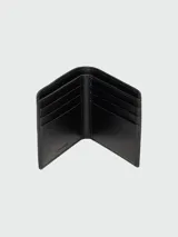 Billetera Marc Jacobs modelo The Billfold, color negro, con diseño plegable de cuero texturizado y estampado frontal en relieve con el texto "The Wallet" y la marca.