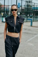 Chaleco de denim oscuro con cuello solapa, cierre frontal con cremallera metálica y bolsillos delanteros con tapeta. Presenta un diseño de corte abullonado con bajo elástico.
