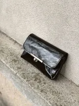Sobre de mano negro con acabado brillante, diseño rectangular con solapa y cierre metálico frontal en tono bronce envejecido.