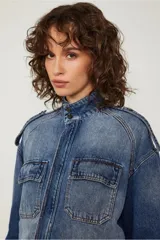 Chaqueta de jean azul con corte oversized, bolsillos con solapa en el frente, cierre metálico y detalles de desgastado suave.