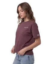 Remera Caterpillar de corte boxy, color marrón oscuro, con cuello redondo y mangas cortas. Presenta un delicado bordado con el logotipo de la marca en el pecho y un parche tejido en la manga.