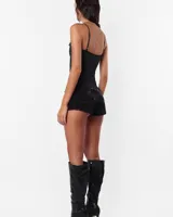 Microshort de jean negro con proceso de sobre teñido y lavado, tiro bajo y corte ajustado. Presenta costuras rojas en toda la prenda, cartera con cierre metálico, presillas largas y detalle de avío en recorte de canesú.