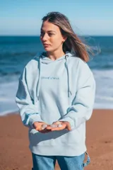 Hoodie celeste con capucha, cordones ajustables, puños y cintura acanalados. Presenta bordado con la frase "Glassy Waves" en el pecho y un diseño de olas en la manga.