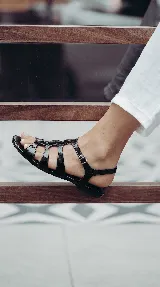 Sandalia plana tipo romana confeccionada 100% en cuero color negro, con múltiples tiras entrelazadas y cierre de hebilla lateral.