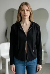 Campera negra de tejido fino con capucha, manga larga y cierre frontal metálico de doble cursor. Presenta un diseño entallado y minimalista.