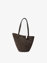 Bolso de mano tipo cubo asimétrico, confeccionado en ante con textura de relieve de cocodrilo. Presenta asas superiores, cierre con anilla metálica plateada y logo de la marca en la parte frontal.