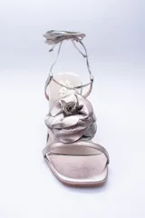 Sandalias de cuero color cobre con taco cuadrado y tira fina sobre los dedos. Presentan una flor grande en el empeine y tiras finas para atar al tobillo.